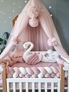 a pink and white baby crib with a swan on it's pillow, stuffed animals and pillows