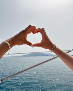 two hands making a heart shape with their fingers on a boat in the ocean,