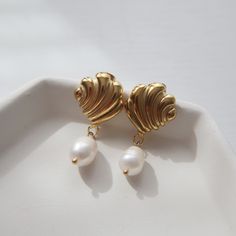 Adorned with a seashell and pearl dangle, these earrings are perfect for adding a beachy and fun flair to any look. -stainless steel, gold plated Shell-shaped Pearl Earrings With Pearl Charm, Shell-shaped Metal Earrings For Gift, Elegant Shell Pearl Earrings For Pierced Ears, Elegant Shell-shaped Earrings, Elegant Shell Pearl Earrings, Elegant Shell-shaped Metal Earrings, Pearl Pendant Drop Earrings In Metal, Pearl Shell Drop Earrings With Pearl Drop Detail, Gold Plated Shell-shaped Earrings