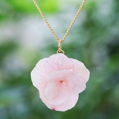 Designed with real flower petals Danai's delicate pendant necklace shimmers with soft colors. The Thai artisan coats pink hydrangea petals with clear glossy resin before suspending the entire pendant from a 22k gold-plated brass rolo chain. Delicate Pink Pendant Flower Necklace, Delicate Pink Flower Pendant Necklace, Pink Flower-shaped Resin Jewelry, Delicate Pink Flower-shaped Necklace, Delicate Pink Flower Shaped Necklace, Pink Flower-shaped Nature-inspired Jewelry, Elegant Pink Pressed Flowers Jewelry, Pink Flower Nature-inspired Jewelry, Pink Resin Jewelry With Pressed Flowers