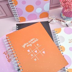 three notebooks are sitting on a table next to a vase with pink and orange flowers