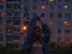 a woman standing in front of a tall building at night with her arms raised up