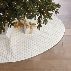 a christmas tree with presents under it on a white round tablecloth and wooden flooring