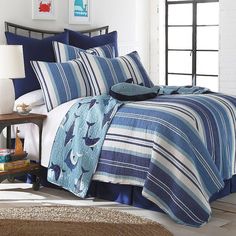 a bed with blue and white comforters in a room next to a lamp on a table