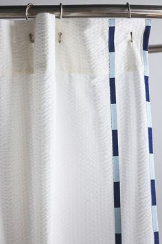 a white shower curtain with blue and white checkerboard fabric hanging from a metal rod