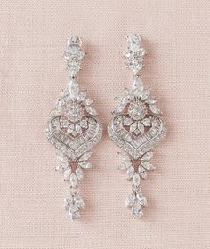 two pairs of diamond earrings on a pink background