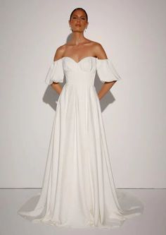 a woman in a white wedding dress standing with her hands on her hips and looking off to the side