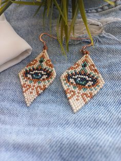 a pair of beaded earrings sitting on top of a piece of cloth next to a potted plant