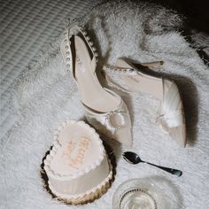 a pair of white high heeled shoes next to a wedding cake on a bed