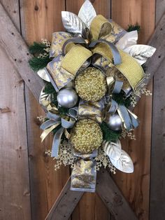 a christmas wreath hanging on the side of a wooden fence with silver and gold decorations