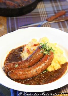 two sausages and mashed potatoes in a white bowl on a plaid tablecloth