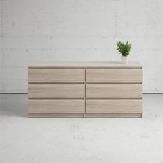 a wooden dresser with a potted plant on top and white wall in the background