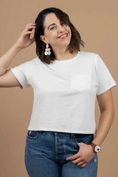 a woman in jeans and a white t - shirt smiles while holding her hand on her head