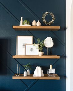 three wooden shelves with books, plants and pictures on them in front of a blue wall