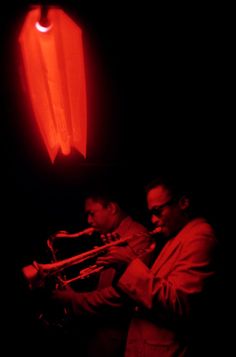 two men playing instruments in the dark with red light shining on their face and behind them