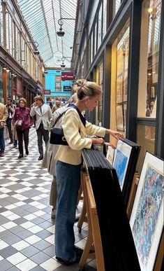 a woman is looking at pictures on display in a building with people walking around it