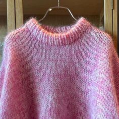 a pink and white sweater hanging on a wooden hanger