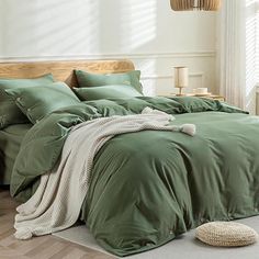 a bed with green sheets and pillows in a room next to a lamp on the floor