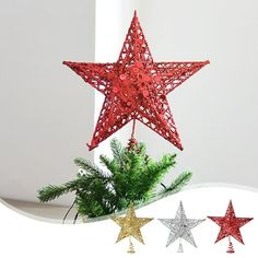 three red and silver stars hanging from the ceiling next to a christmas tree with pine branches