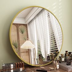 a round mirror sitting on top of a wooden table next to a lamp and bottles