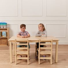 two children sitting at a wooden table in front of bookshelves on the floor