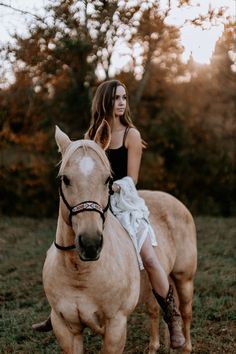 a young woman riding on the back of a brown horse in a grassy field next to trees