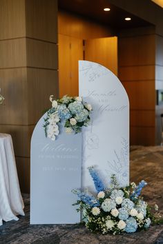 a white and blue wedding sign with flowers on it in front of a table cloth