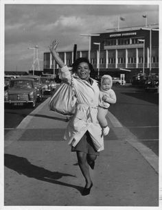 a black and white photo of a woman holding a baby in her arms while walking down the street