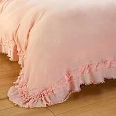 a pink comforter with ruffles on the bottom and sides is sitting on a wooden floor