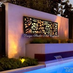 an outdoor swimming pool at night with lights on the wall and planters around it