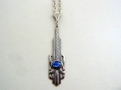 a silver necklace with a blue stone in the center on a white surface, hanging from a chain