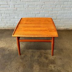 a small wooden table sitting in front of a brick wall on concrete floored area