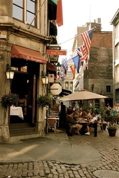 people are sitting at tables in the middle of an alleyway with flags flying overhead