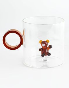 a glass cup with a red handle and a brown teddy bear on the inside, sitting in front of a white background