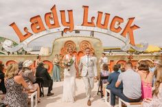 Witness the joy as this couple walks hand in hand, just married, under a glowing "Lady Luck" neon sign 🎉. The bride dazzles in a timeless wedding dress with a plunging neckline and delicate beading 🌟, while the groom rocks a light summer suit. Perfect inspo for unique wedding ideas 💡. Catch the vibes of this lively neon museum wedding! #weddingideas #weddingdress #uniqueideas #summerweddings #neonwedding Unique Wedding Ideas, Summer Suit