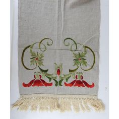 an embroidered wall hanging with red flowers and green leaves on white fabric, next to a tasseled fringe