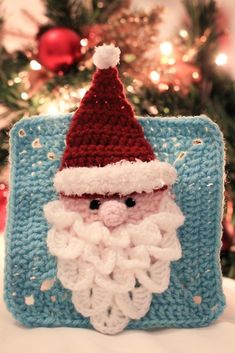 a crocheted santa clause sitting on top of a blue blanket next to a christmas tree