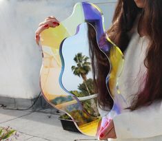 a woman is holding a large colorful piece of art in front of her face and palm trees behind her