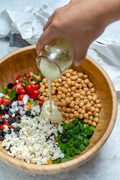 a person pouring dressing over a salad in a bowl with chickpeas and tomatoes