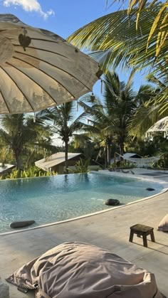 an open umbrella sitting next to a swimming pool with lounge chairs and palm trees in the background