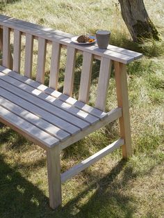 a wooden bench sitting in the grass next to a tree with a bowl of food on it