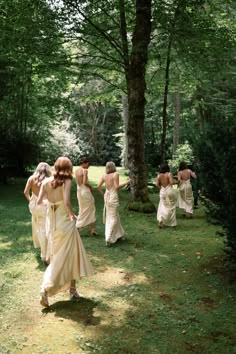 a group of women in long dresses walking down a path next to a large tree