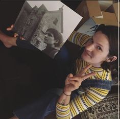 a woman sitting on the floor holding up two pictures and pointing to her left side