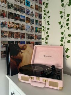 a record player sitting on top of a pink suitcase next to a wall covered with pictures