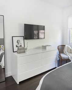 a bedroom with white furniture and a flat screen tv mounted on the wall above it