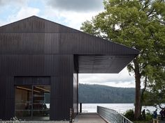 a black building sitting on the side of a lake next to a wooden walkway and trees