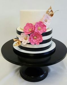 a white and black striped cake with pink flowers on the top is sitting on a stand