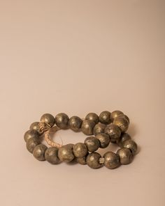 These brass African beads are beautifully textured, each individual bead unique in shape and finish for a final look that feels one-of-a-kind and natural. Perfect for layering on a vase, an open book, a bowl, or styling on a shelf. All Sales Final Free Shipping Artisan Brass Jewelry With Round Beads, Artisan Gold Bracelets With Polished Beads, Gold Artisan Bracelet With Polished Beads, Rustic Large Beads For Gifts, Artisan Brass Jewelry With Large Beads, Bronze Polished Round Bead Jewelry, Artisan Gold Bracelets With Wooden Beads, Artisan Bronze Jewelry With Polished Beads, Bronze Beaded Necklaces With Large Beads For Gift