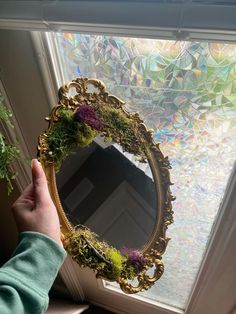 a person is holding up a mirror with plants in the frame and moss growing on it