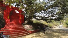 a person walking down a dirt road next to a red building with steps leading up to it